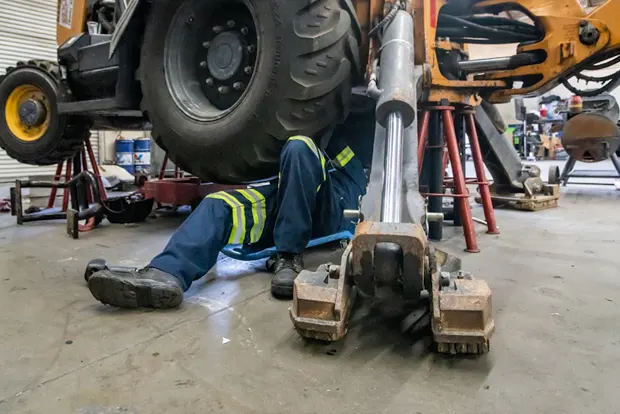 Mechanic working underneath heavy machinery in a garage setting.