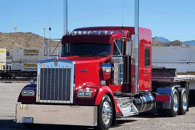 Red semi-truck parked in industrial area with shipping containers.