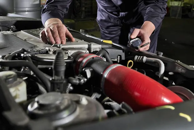 Mechanic examining a vehicle engine with a large red air intake tube.