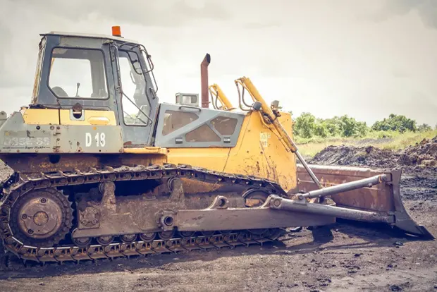Bulldozer on muddy ground with overcast sky in the background.