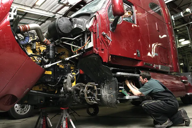 Mechanic working on the engine of a large red truck in a garage.