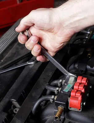 Hand using a wrench on red engine components.