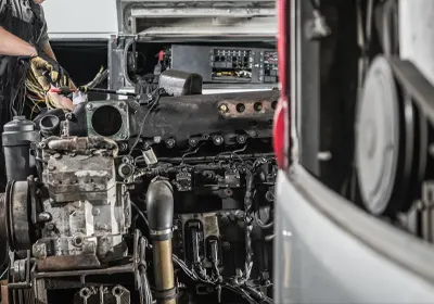 Mechanic working on a disassembled diesel engine in a workshop.